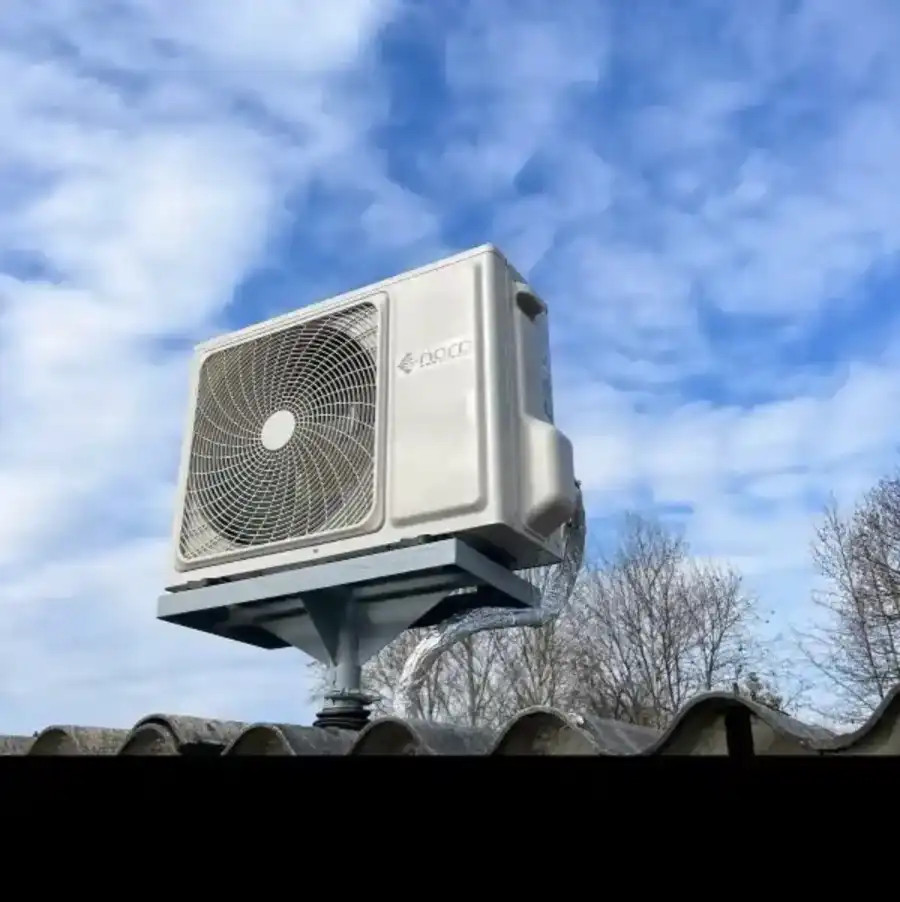 Kültéri klímaberendezés kültéri egysége ventilátorral, kék ég és fák között, felhős háttérrel.